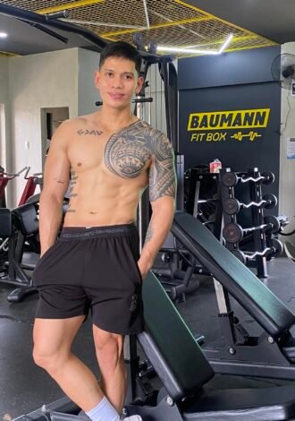 Patrick Baumann, owner and coach at Baumann Fit Box, posing in the gym with fitness equipment and the gym’s logo in the background.