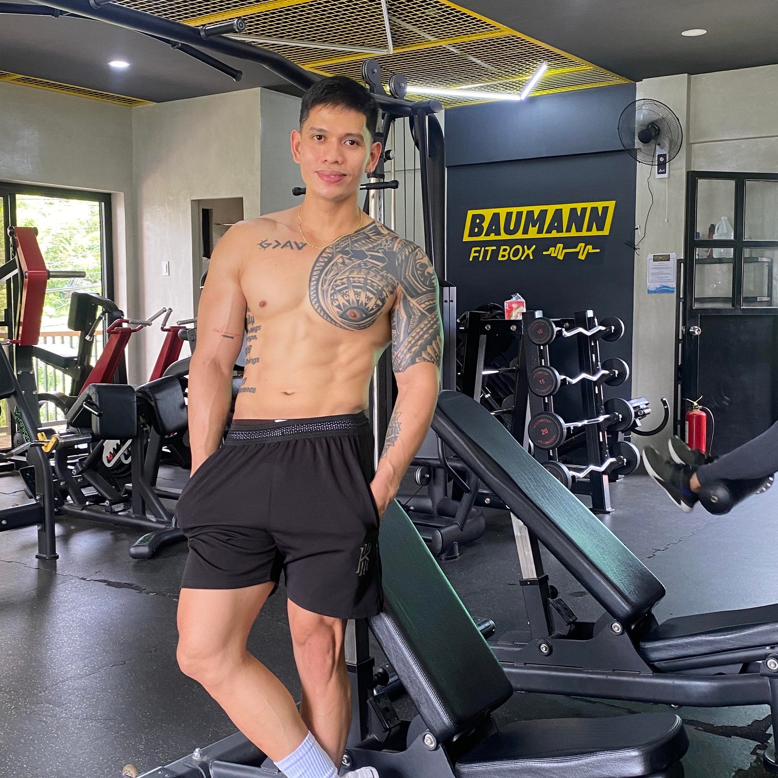Patrick Baumann, owner and coach at Baumann Fit Box, posing in the gym with fitness equipment and the gym’s logo in the background.