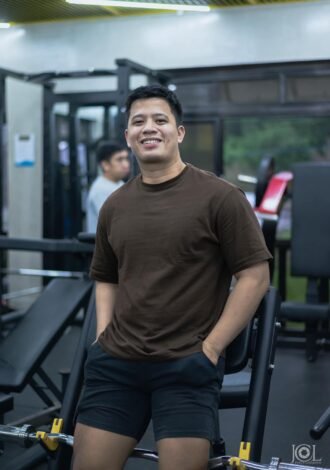 Marc Lalap, coach at Baumann Fit Box, smiling and posing inside the gym, surrounded by fitness equipment and an energetic training environment.
