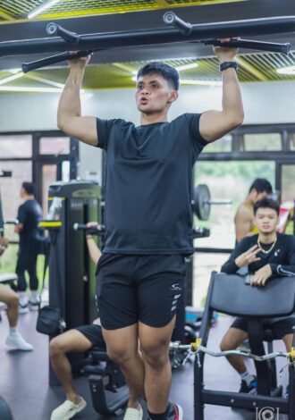 Aaron Noche, coach at Baumann Fit Box, performing a pull-up during a training session in the gym, surrounded by an active and motivating fitness environment.